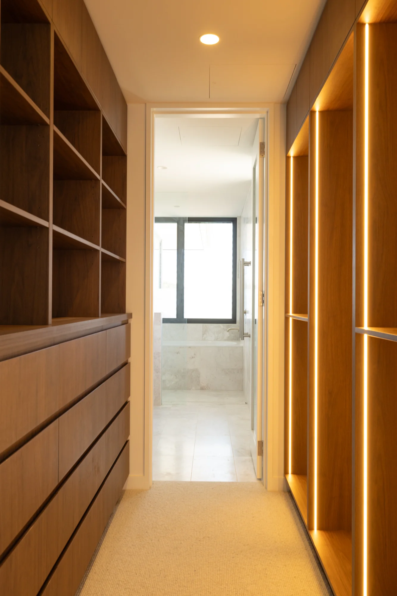 Empty Ettalong walk-in wardrobe with timber-tone drawers, open shelves and illuminated hanging sections
