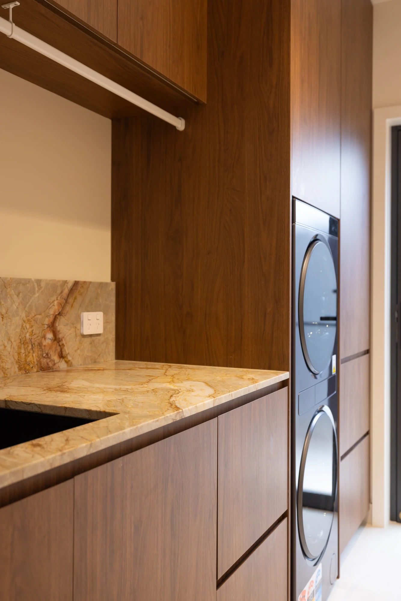 Detail of Solara House laundry cabinetry around stacked appliances, drawers and a hanging rail