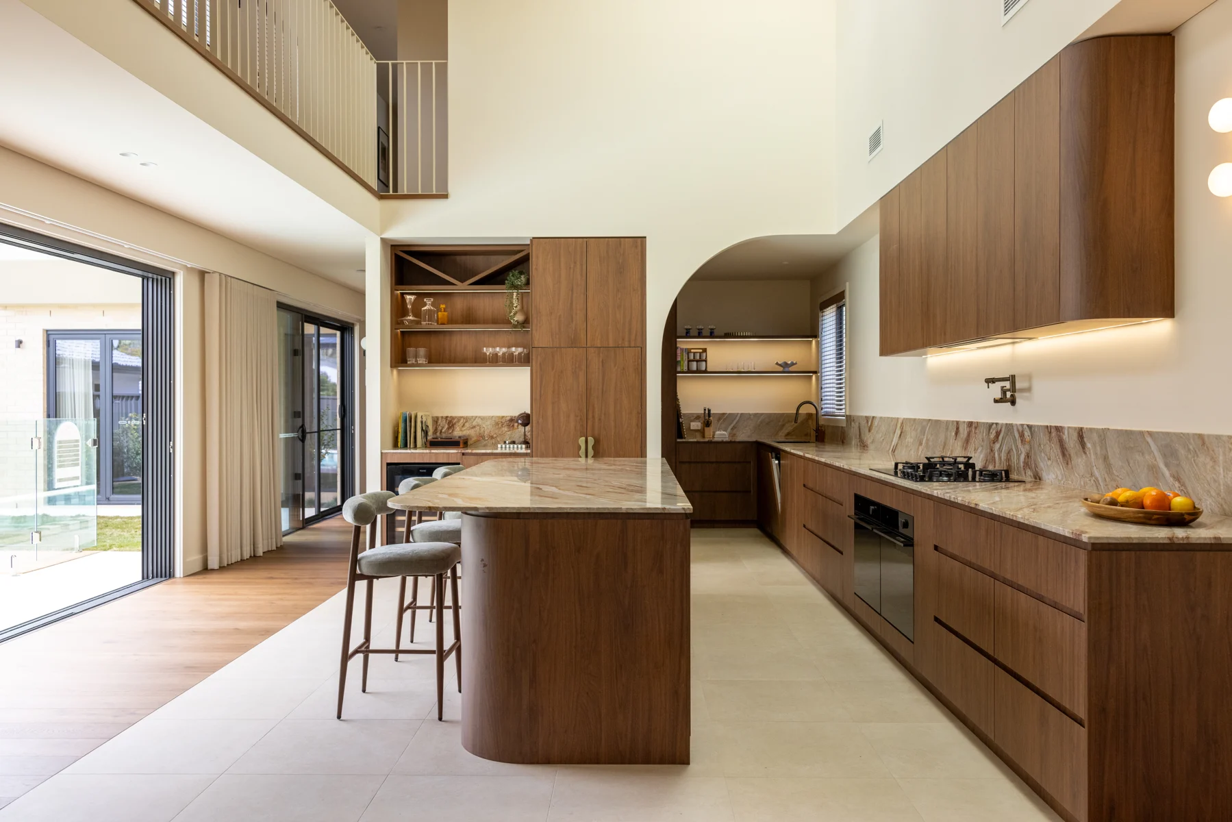 Solara House kitchen at Long Jetty with timber-tone cabinetry, curved island and arched pantry opening
