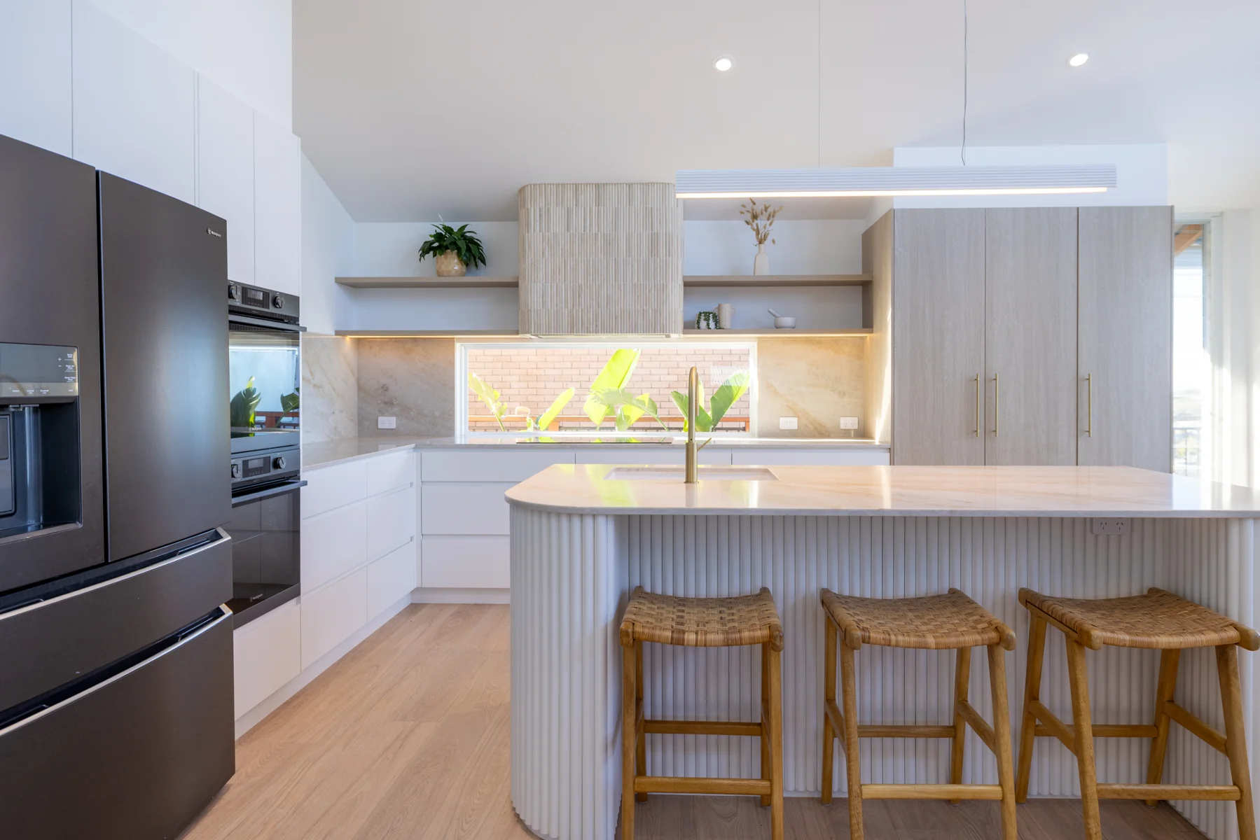 Wamberal kitchen with light cabinetry, fluted island front, seating and an integrated rangehood